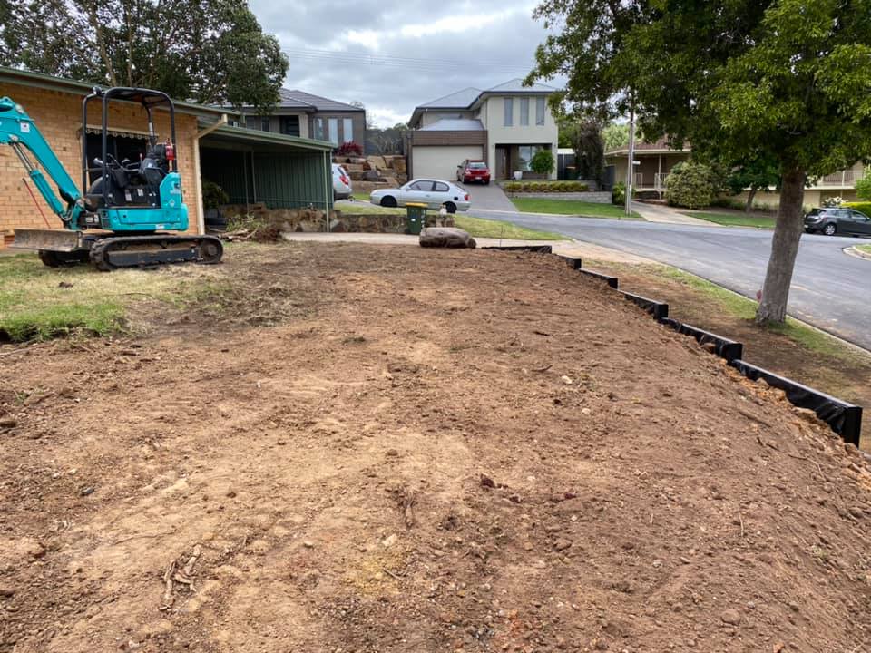 Mini excavator on a freshly cleared sloping block beside a suburban street