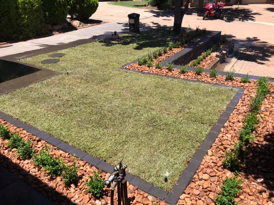 Front garden with new turf framed by dark edging and red rock garden beds